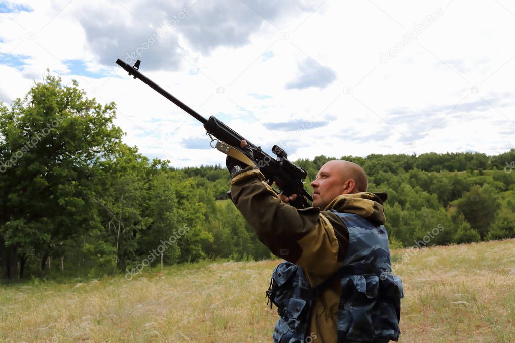 Hunting season. Male 35-40 years old, a hunter is aiming at the sky from a firearm in a clearing in the forest.