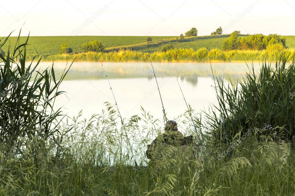 Summer sunny landscape. Morning, dawn on the lake. A fisherman sits on the shore with a fishing rod. Saratov Region, Russia.