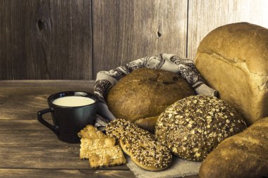 Rustik natürmort. Gıda. Taze ekmek ürün yelpazesine bir ekmek, bisküvi ve ahşap masa arka plan üzerinde süt ile bir kupa pişmiş