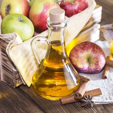 Kırmızı ve yeşil elma tarımsal bir ürün işleme. Evde konserve, sağlıklı diyet vejetaryen yemek. Baharatlı elma elma şarabı sirke, meyve suyu, bir sandık dolusu olgun meyve yanındaki cam sürahi içinde tarçınlı elma şarabı