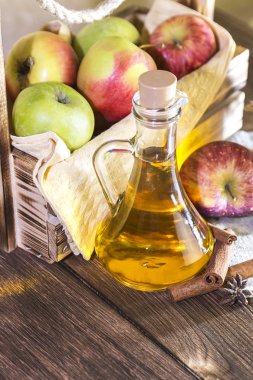 Kırmızı ve yeşil elma tarımsal bir ürün işleme. Evde konserve, sağlıklı diyet vejetaryen yemek. Baharatlı elma elma şarabı sirke, meyve suyu, bir sandık dolusu olgun meyve yanındaki cam sürahi içinde tarçınlı elma şarabı