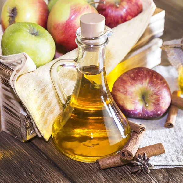 Kırmızı ve yeşil elma tarımsal bir ürün işleme. Evde konserve, sağlıklı diyet vejetaryen yemek. Baharatlı elma elma şarabı sirke, meyve suyu, bir sandık dolusu olgun meyve yanındaki cam sürahi içinde tarçınlı elma şarabı