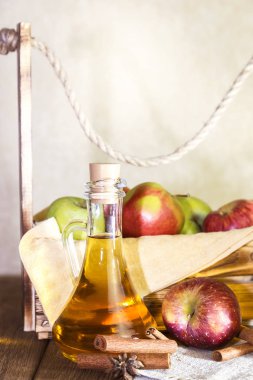 Kırmızı ve yeşil elma tarımsal bir ürün işleme. Evde konserve, sağlıklı diyet vejetaryen yemek. Baharatlı elma elma şarabı sirke, meyve suyu, bir sandık dolusu olgun meyve yanındaki cam sürahi içinde tarçınlı elma şarabı