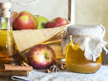 Kırmızı ve yeşil elma tarımsal bir ürün işleme. Evde konserve, sağlıklı diyet vejetaryen yemek. Baharatlı elma elma şarabı sirke, meyve suyu, olgun meyve kutusunun yanındaki cam kavanozda tarçınlı elma şarabı