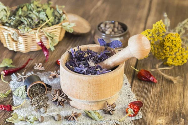 Fragrant dried healing herbs for therapy and spicy spices. On the table in a mortar are purple basil, tansy, pepper, chili and cardamom, in a rustic style.