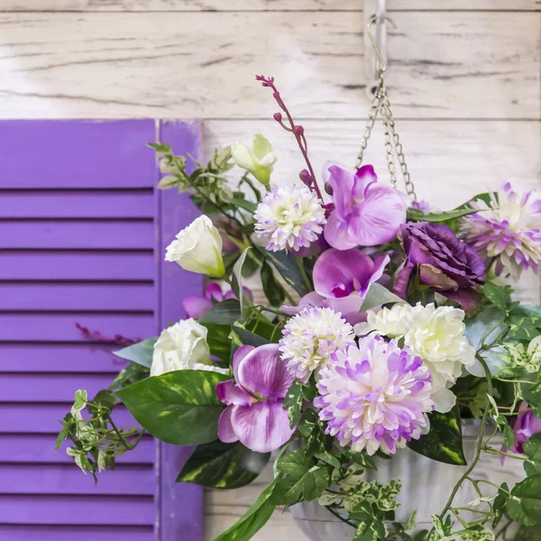 Garden design and decor to decorate the exterior of the facade of the house. A bouquet of different colors of purple hanging in a pot on the wall by the window