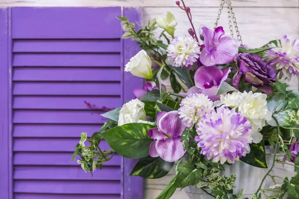 Garden design and decor to decorate the exterior of the facade of the house. A bouquet of different colors of purple hanging in a pot on the wall by the window