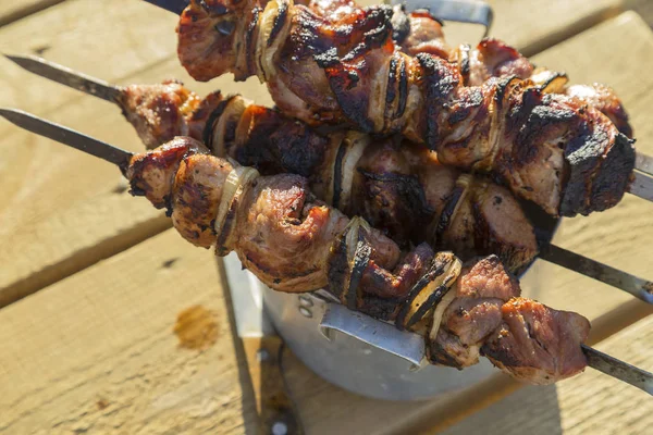 Food on the fire, picnic. Cooked grilled fragrant delicious hot grilled shashlik barbeque on coals on the grill of marinated pork, lamb and beef with onions on skewers on the table — Stock Photo, Image