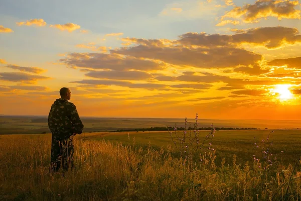 Human and nature. A European man stands in a field, looking into the distance to the horizon and enjoying the view of the landscape at sunrise or sunset. The orange sky and the sun in the morning, in the evening in Russia in the Saratov region