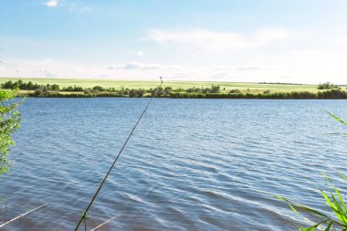Mavi gökyüzüne karşı güzel bir mavi göl ve yeşil alanlar ile yaz manzara. Yürüyüş, gölette balık tutmak. Sıcak bir günde nehre yolculuk