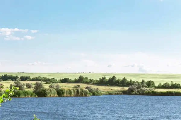 Zomer landschap met een prachtig blauw meer en groene velden tegen een blauwe hemel. Wandelen, vissen op de vijver. Reis naar de rivier op een warme dag — Stockfoto