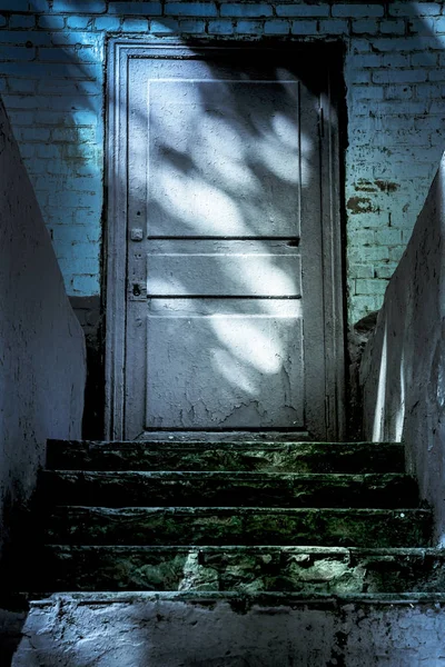 Mörker och fasa vid den stängda entrédörren till spökhuset. Mörk sten förstörde gamla trappan från källaren med mystiska skuggor och konstiga ljus — Stockfoto