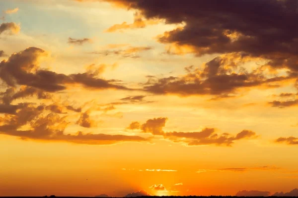 Beautiful bright majestic dramatic evening sky at sunset orange color with rays. The sun shines over the horizon against the backdrop of thunderclouds at dusk