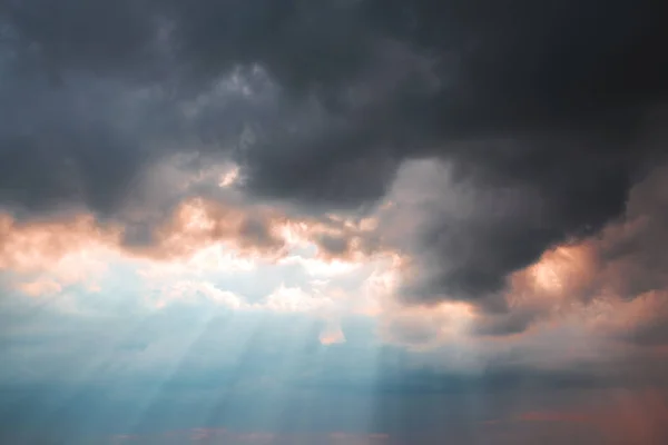 Heavenly dramatic landscape background. Bad weather, thunderstorm, clouds, storm. The concept of the struggle of light and darkness. The shining of the sun\'s rays in the blue sky through the black clouds in the evening at sunset