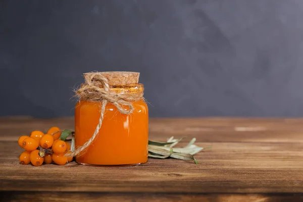 Produção caseira de frutas enlatadas e bagas, suco, óleo essencial de frutos maduros de espinheiro do mar em um jarro de vidro em um fundo de madeira, estilo rústico escuro. Comida doce, sobremesa — Fotografia de Stock