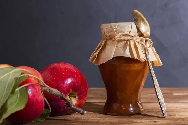 Homemade production, canning, jam jam in a glass jar with a spoon on a wooden background in a rustic style and ripe red fresh fruits. Homemade food, dessert, sweet food