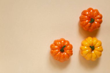 Cadılar Bayramı sonbaharı bej bej kaplama arka plan. Bej bir yüzeyde üç turuncu ve sarı balkabağı ve bir kopya alanı olan kumaş dokusu.