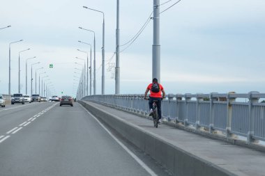 Saratov bölgesi, Rusya - 05 / 22 / 2020: Yazın öğleden sonra sokakta bisiklet süren yetişkin bir adam Engels Köprüsü üzerinde bisiklet sürüyor. Aktif sağlıklı yaşam tarzı, kentsel alanda açık hava sporları hobisi