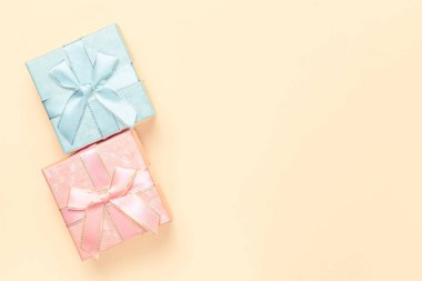 Hediye paketi, iki güzel pembe mavi kutu, bayram için kurdelelerden gelen kurdeleler, pastel renklerle bej şeftali arkaplan, fotokopi alanı üst görünümü, düz çizgi.