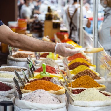 Doğu pazarında çantalarda çeşitli doğal kokulu Asya Hint baharatlarının satışı, bir adamın eldiven içindeki eli bir mağaza vitrinindeki bir kepçenin içinde mal satıyor.