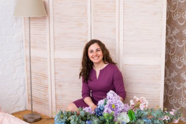 Çiçekler ve görünüyor kamera tutan güzel kadın. Genç kadın, çiçek yanında, iç ev. Gülümseyen mutlu ev kadını evde çiçek ile. Esmer saçlı gülümseyen kadın.