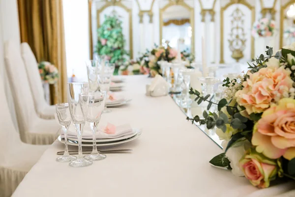 Table served for newlyweds dinner in luxury restaurant. White candles, cutlery on mirror, decorations with flowers. Nobody.