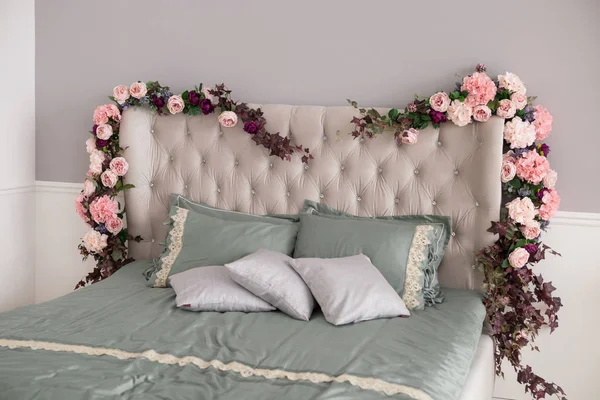 Stylish bedroom interior design with flowers, white and gray pillows on bed. Home interior design real photo of luxury bed.