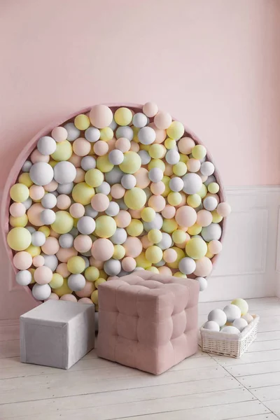 Photo zone with pouf and colorful balls on wall. Pink, gray and yellow balls on wall, soft colors.