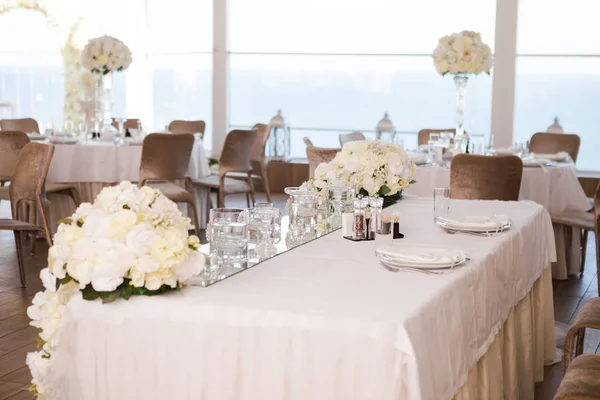 Table set for wedding reception with flowers, white tablecloth, crystal glasses and cutlery, nobody.