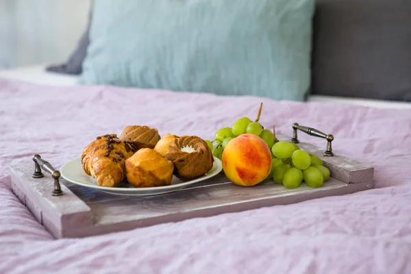 Breakfast on tray in bed, cozy home atmosphere. Breakfast in bed, tray with fruits and croissants, close up shot.