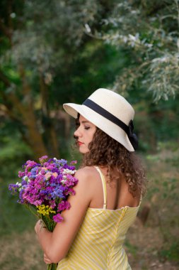 Genç kadın çiçek el ve kafasındaki beyaz şapka ile. Yaz Park, kıvırcık saçlı çekici kadın arkadan görüntüleyin. Kadının gün kavramı.