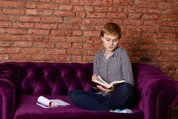 Студент читает книгу сидя на диване . — стоковое фото