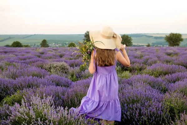 Woman in purple dress and hat in lavender field.