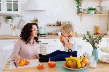 Küçük çocuk masada oturmuş portakal yiyor..