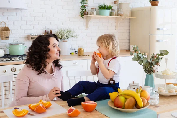 Little boy eating orange sitting on table. — Stock Photo, Image