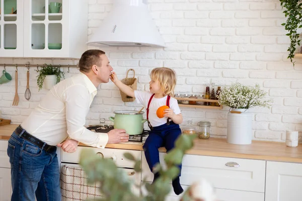 Son feeds father in the kitchen. — Stock Photo, Image