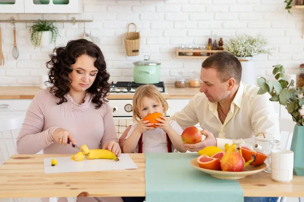 Smiling son eating orange with parents. — Stock Photo, Image