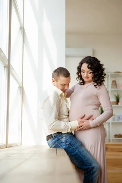 Pregnant woman with husband stands near window. — Stock Photo, Image