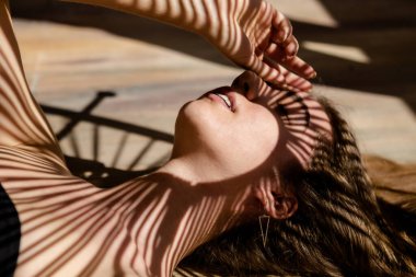 Yüzünde palmiye yaprağı gölgeleri olan güzel bir kadın modelin portresi. Güneşlenme, tatil, rahatlama kavramı.