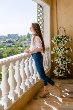 Güneşli bir günde terasta çay içen bir kadın. Genç bir kadın sabah vakti balkonda dinleniyor..