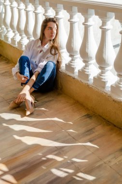 Terasta oturan ve esnek bir kadın, güneşli bir gün. Beyaz gömlek ve mavi kot giyen genç bir kadın, yüksek tepeler..