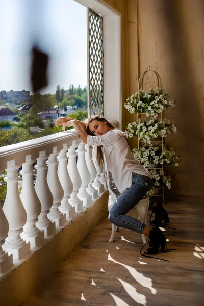 Terasta oturan genç çekici bir kadın, hafta sonu konsepti ve yaz tatilinde dinlenmek. Mavi kot ve beyaz gömlek giyen siyah saçlı kadın. Lüks daire..