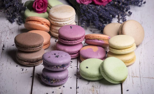 colorful macaroons with roses and lavender flowers on wooden background