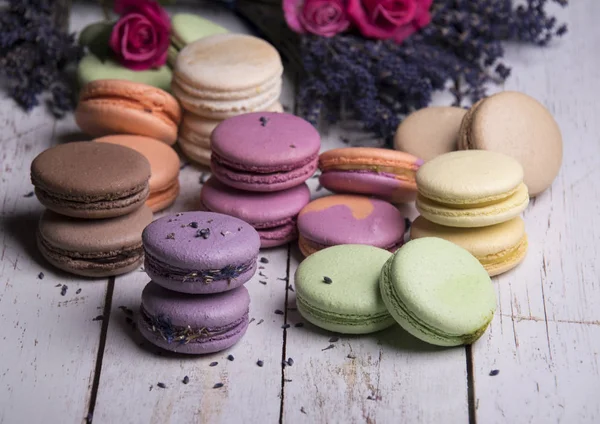 colorful macaroons with roses and lavender flowers on wooden background