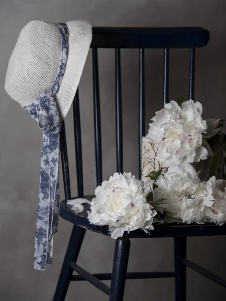 hat hanging on wooden chair and white peony flowers