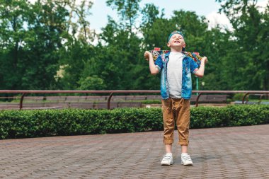 Bir küçük şehir çocuğu ve bir kaykay. Genç bir adam parkta duran ve bir kaykay tutarak. City Style. Şehir çocukları. Bir çocuk bir kaykay binmek öğrenir
