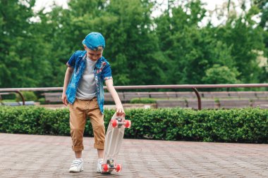 Bir küçük şehir çocuğu ve bir kaykay. Genç bir adam bir parkta bir kaykay üzerinde biniyor. City Style. Şehir çocukları. Bir çocuk bir kaykay binmek öğrenir