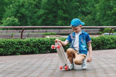 Bir küçük şehir çocuğu ve bir kaykay. Genç bir adam bir parkta bir kaykay üzerinde biniyor. City Style. Şehir çocukları. Bir çocuk bir kaykay binmek öğrenir