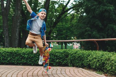 Bir küçük şehir çocuğu ve bir kaykay. Genç bir adam bir parkta bir kaykay üzerinde biniyor. City Style. Şehir çocukları. Bir çocuk bir kaykay binmek öğrenir