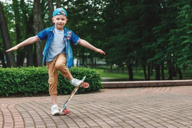 Bir küçük şehir çocuğu ve bir kaykay. Genç bir adam bir parkta bir kaykay üzerinde biniyor. City Style. Şehir çocukları. Bir çocuk bir kaykay binmek öğrenir